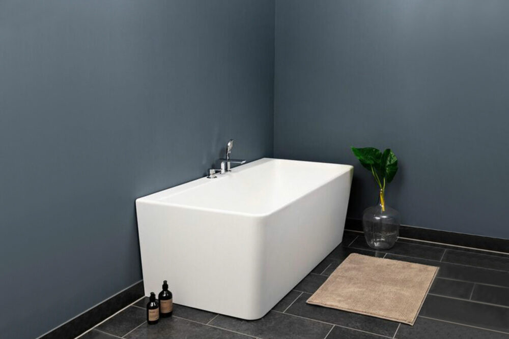 Saga Back To Wall er et stilrent badekar i silkemyk, matt kompositt. Den ergonomiske utformingen gjør det svært behagelig å sitte i. God plass for å montere armatur på badekaret. Leveres med klikkventil og justerbare ben. mørke fliser og flott blå veggfarge